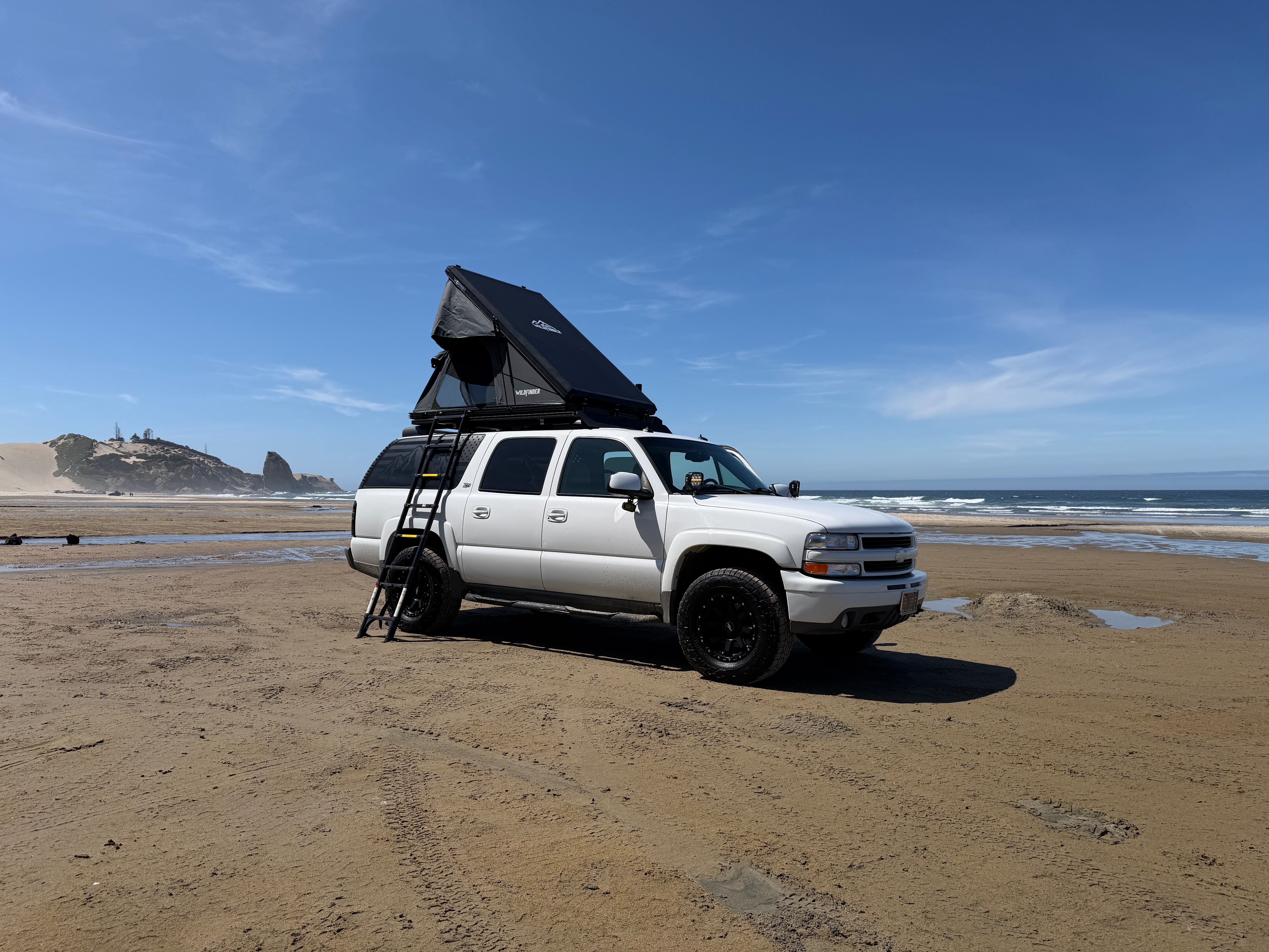 White GMT800 Chevrolet Suburban Z71 with a rooftop tent parked on an Oregon beach